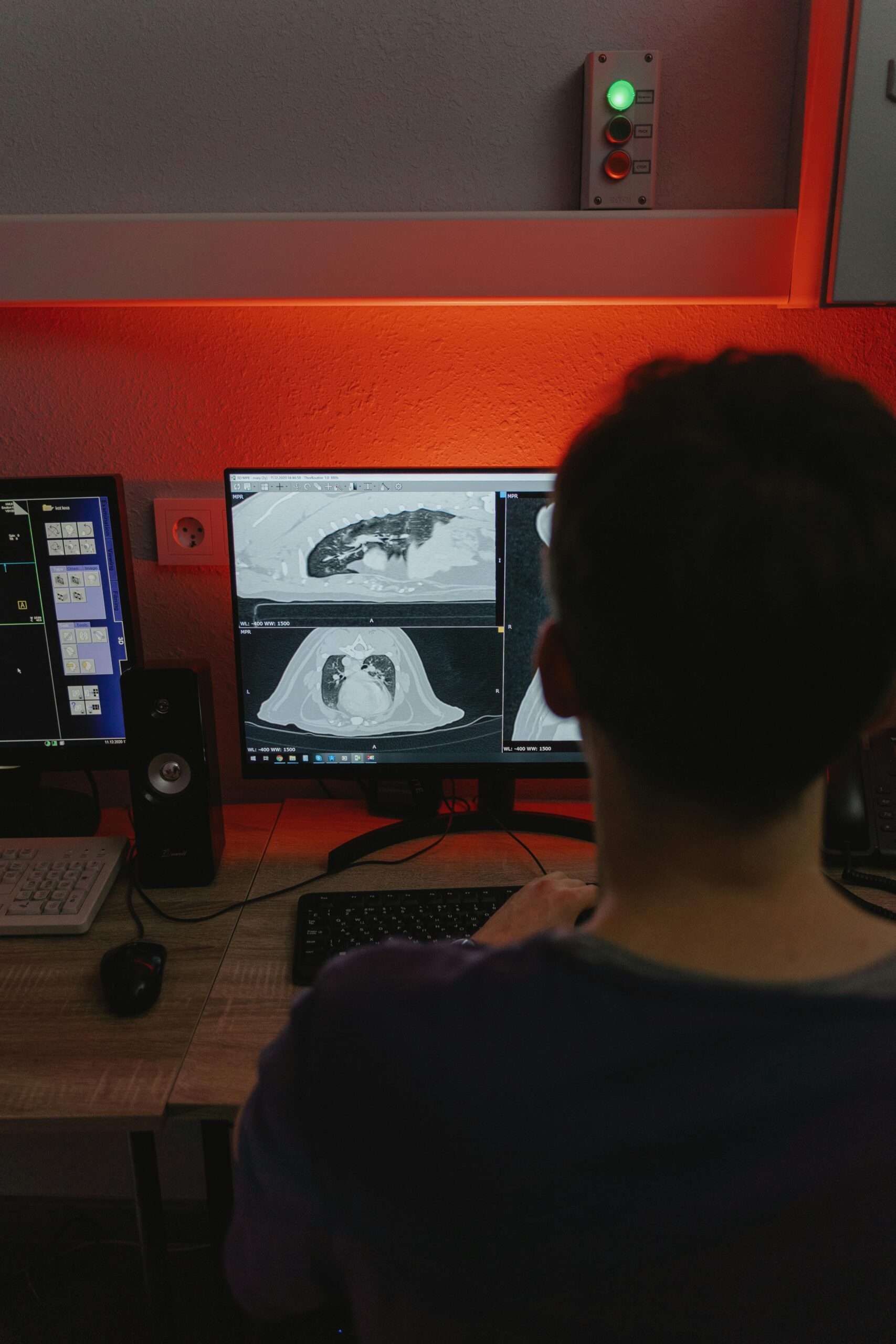 A medical professional studies CT scans on multiple monitors in a dimly lit medical office.